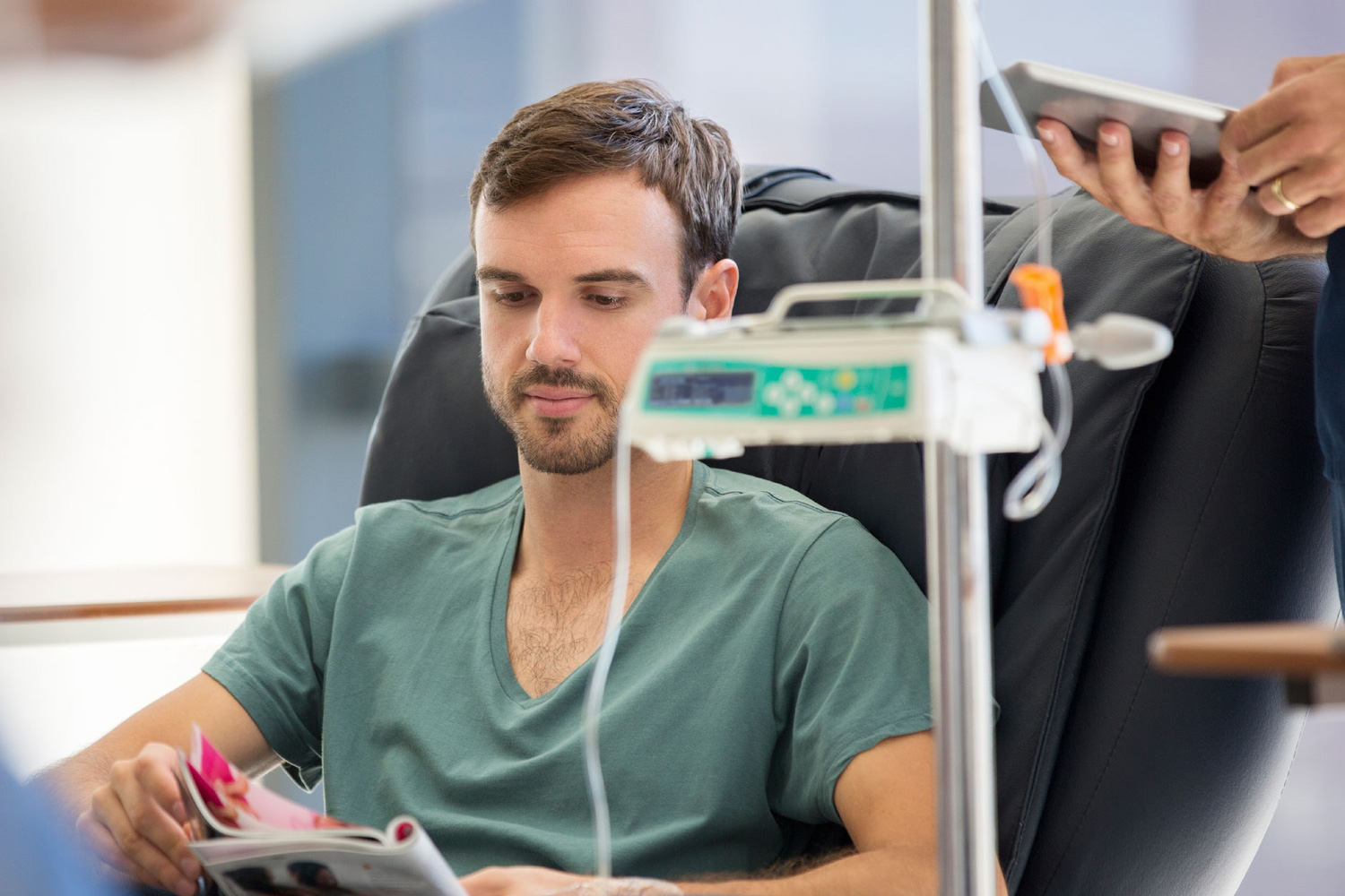 Mann in einem Infusionssessel liest ein Magazin, Infusionsger&auml;t daneben